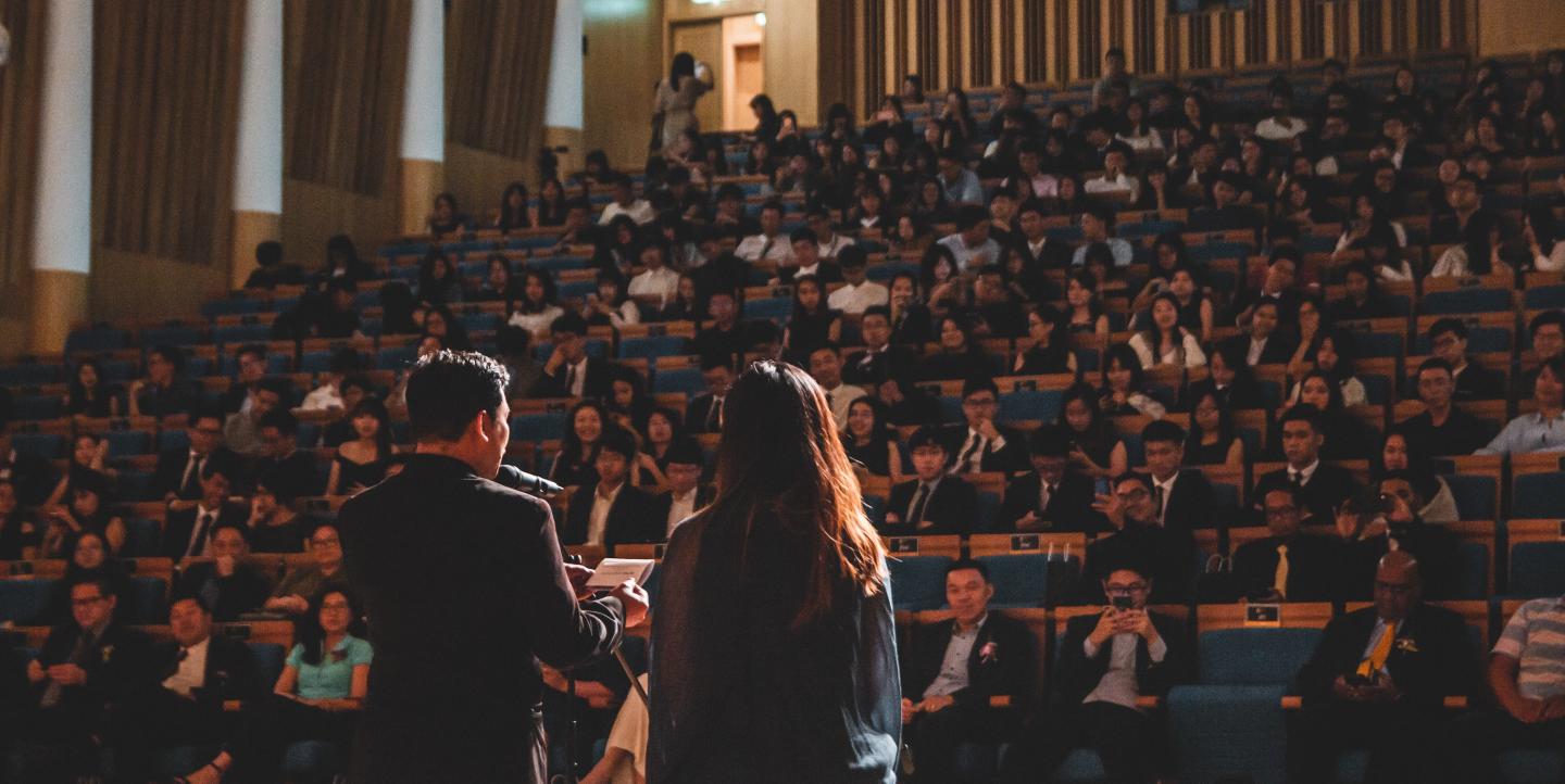 An auditorium full of people listening to two people speak on stage.