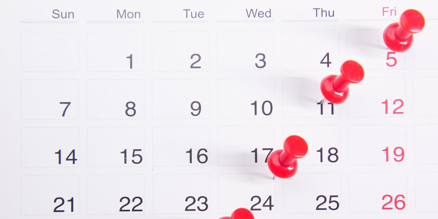 Un calendrier noir et blanc, avec des punaises rouges pour marquer certaines dates