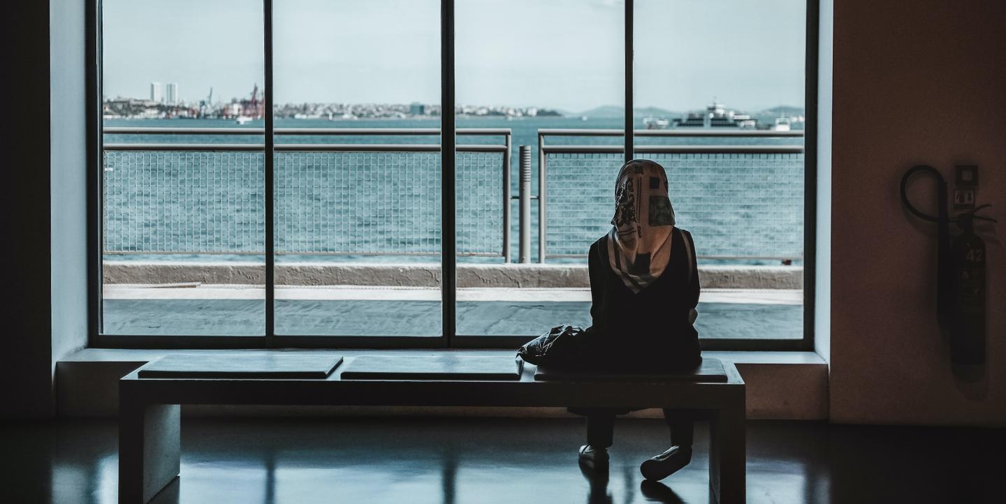 Woman sits alone looking out a large window