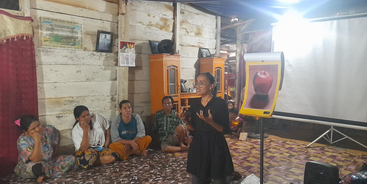 Zulfa in front of an image of an apple speaking to a group of people sitting on the floor