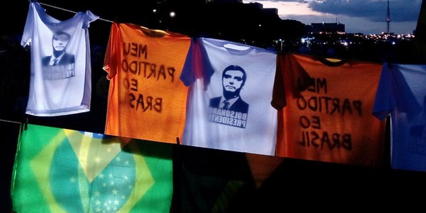 Camisetas com o rosto de Bolsonaro penduradas juntas com a bandeira do Brasil