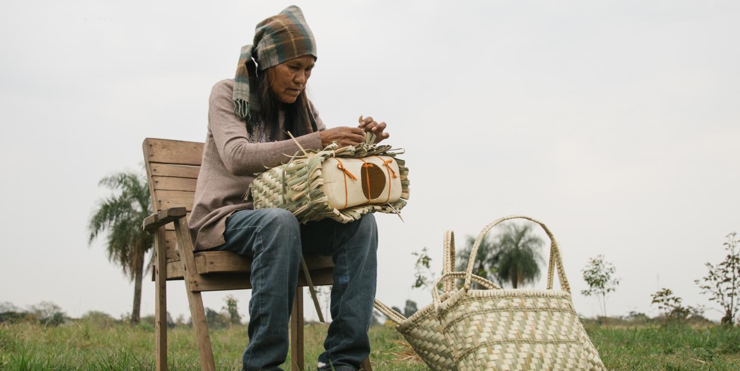 Indígena sentada em banco fazendo sacolas
