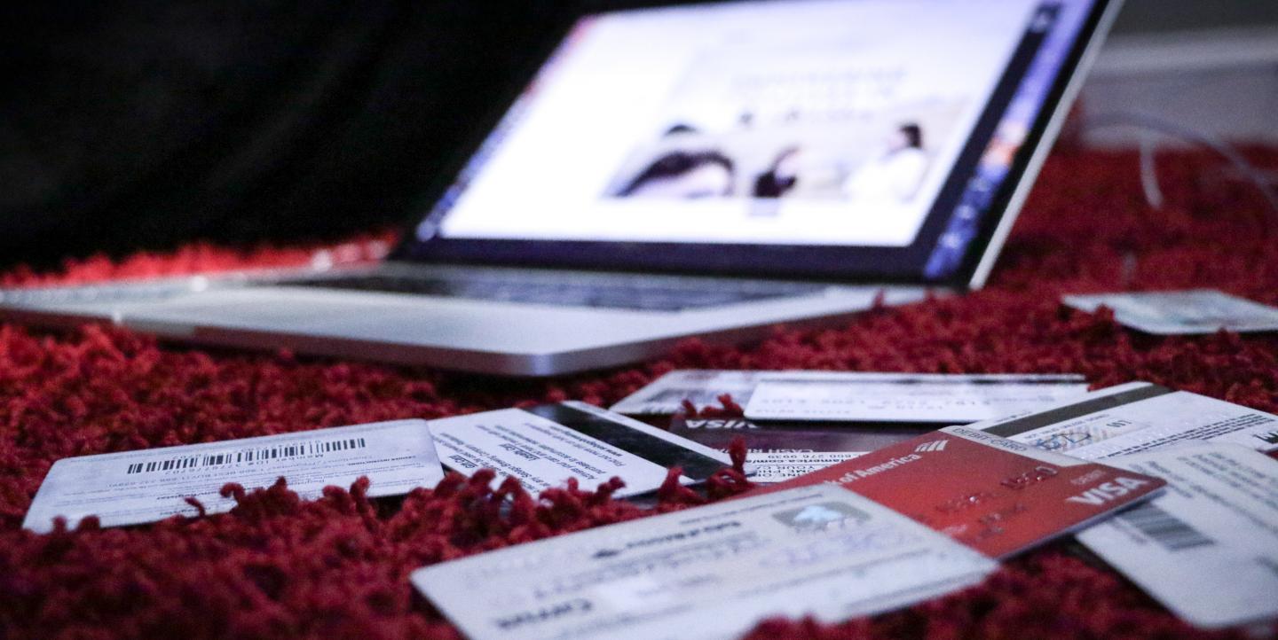 A laptop computer sits open on a red, fuzzy rug surrounded by credit cards