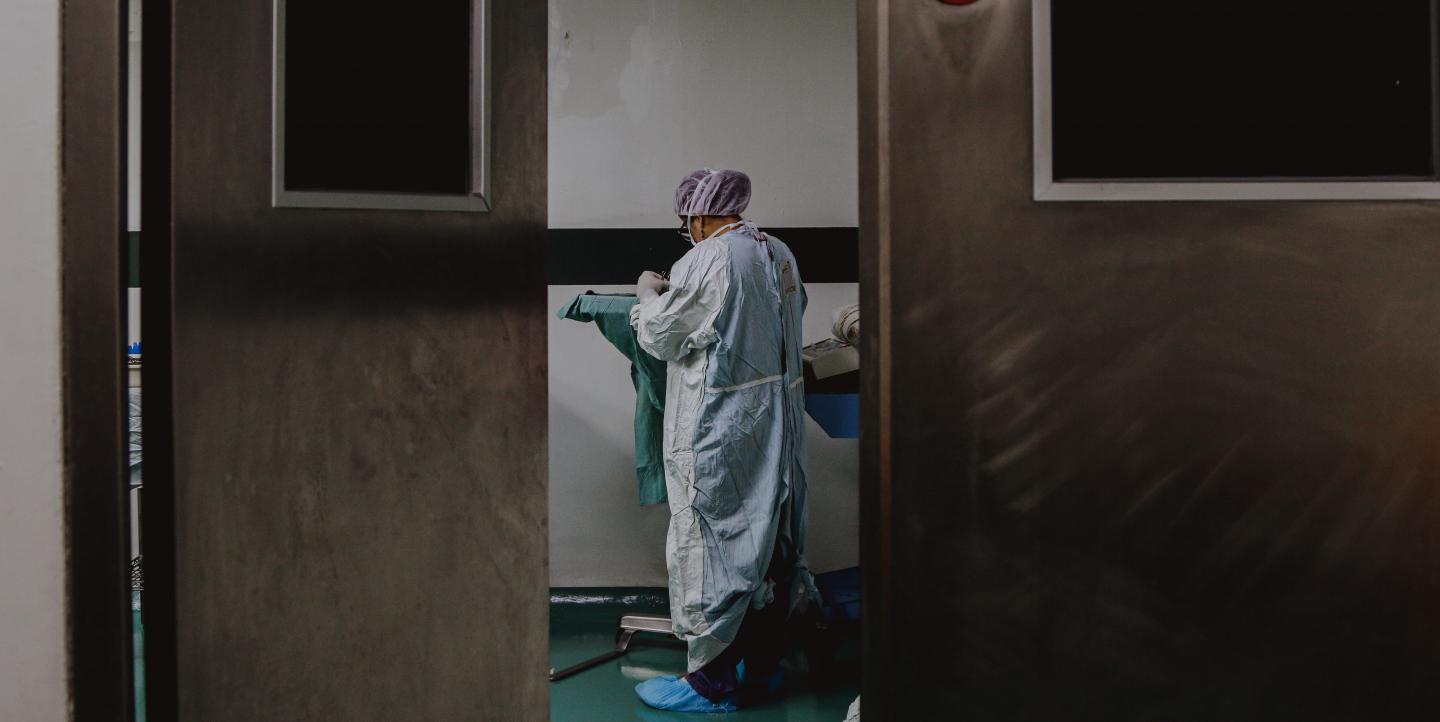 Porta entreaberta mostrando pessoa vestida com jaleco e touca em hospital na República Dominicana