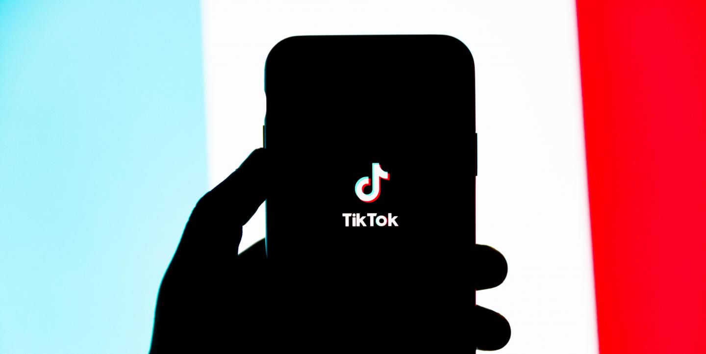 Sombra de uma mão segurando um telefone com o logo da TikTok