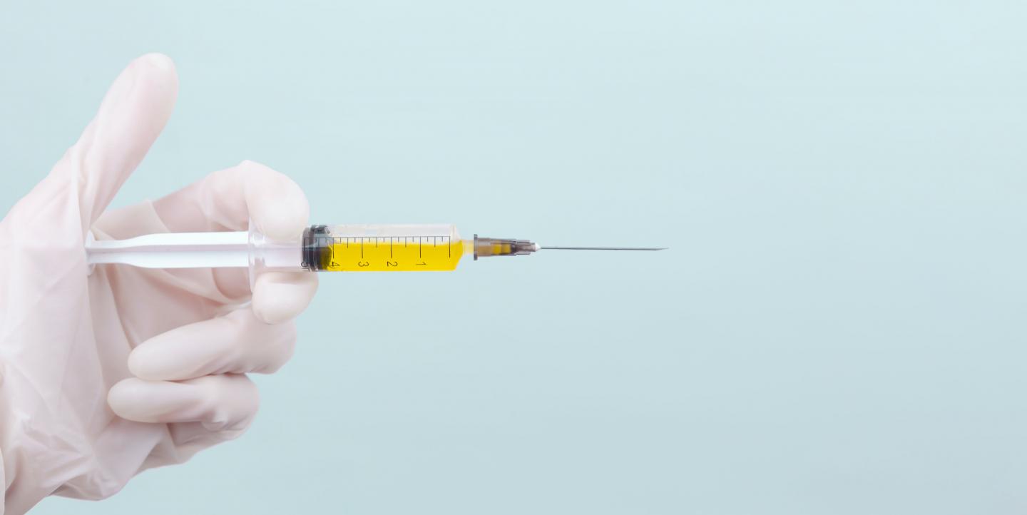 A white glove holding out a syringe full of yellow liquid