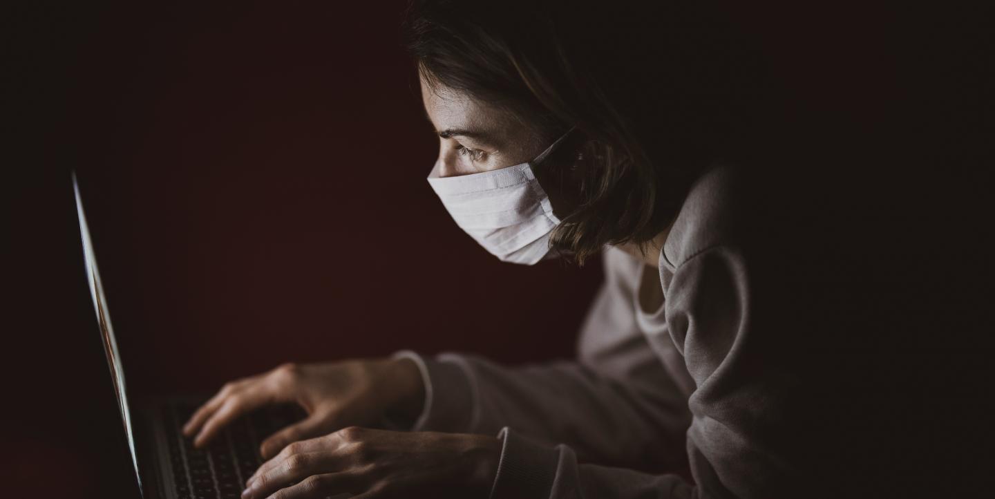 Une personne sur son ordinateur avec un masque