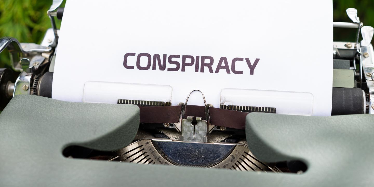 A typewriter with a paper sticking out of it that says conspiracy.