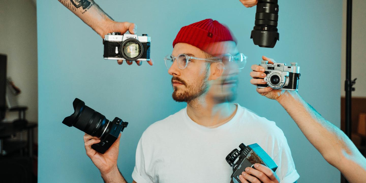 Un photographe, sur fond bleu, avec de multiples appareils photo