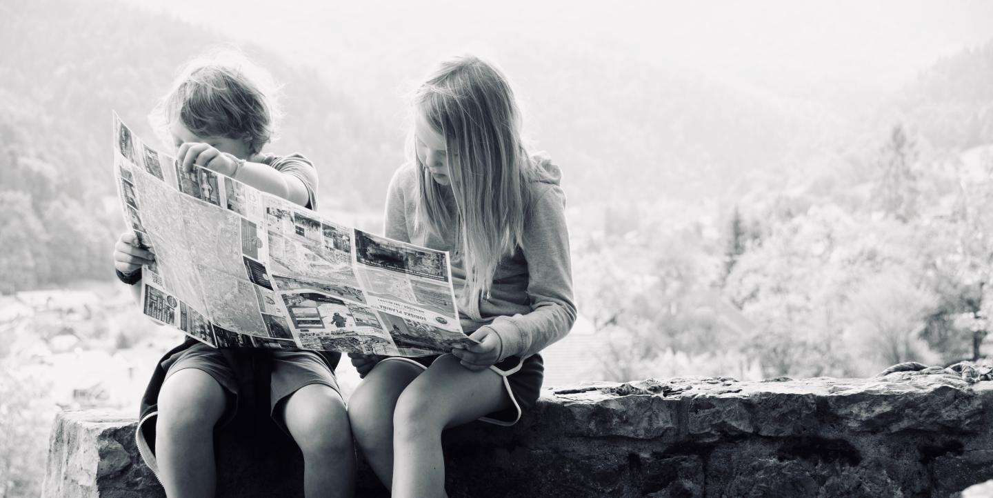 Two Children in greyscale reading a newspaper