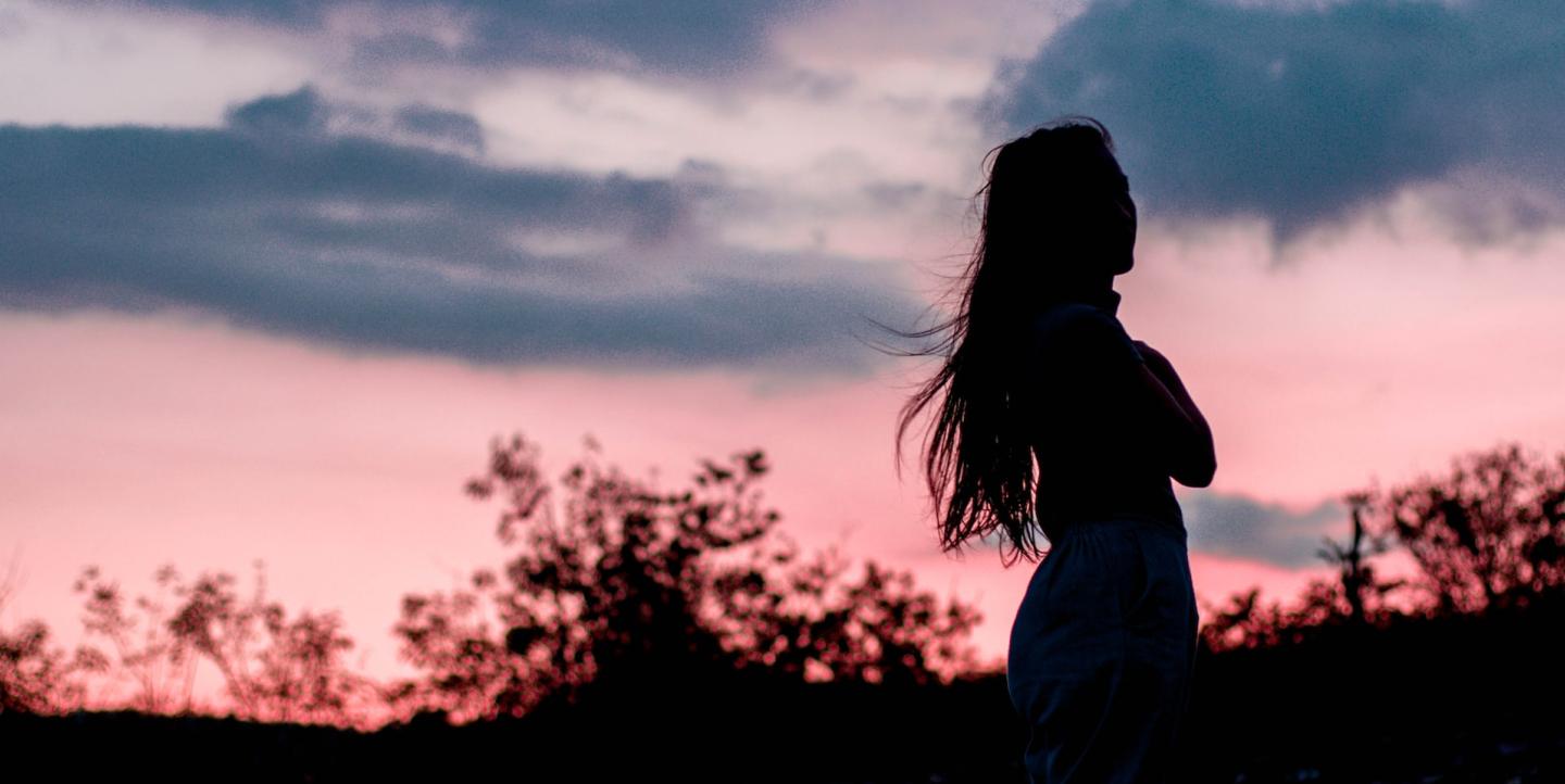 Темный силуэт женщины на фоне закатного неба