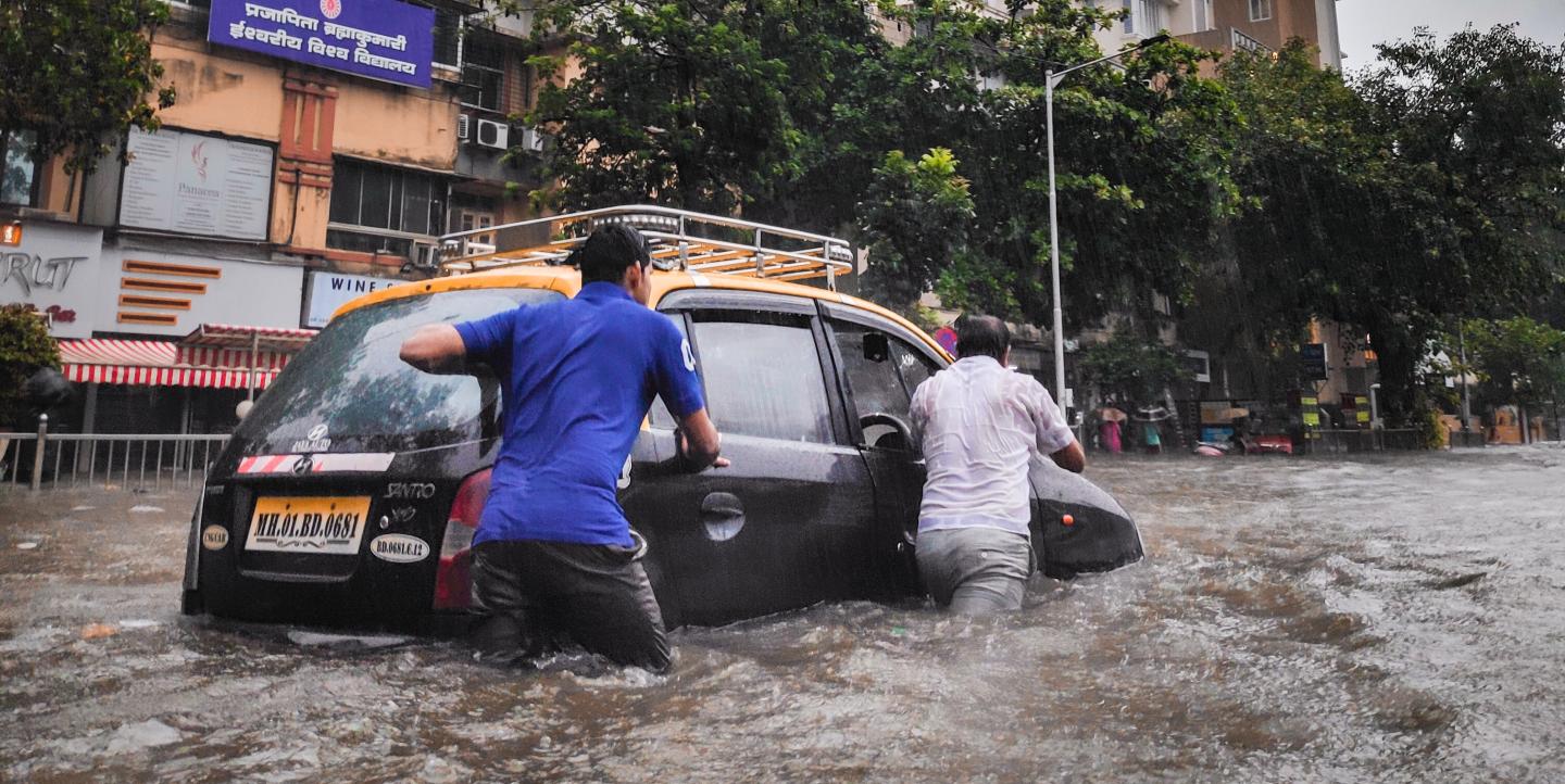 Deux hommes poussent une voiture, au milieu d'une rue inondée 