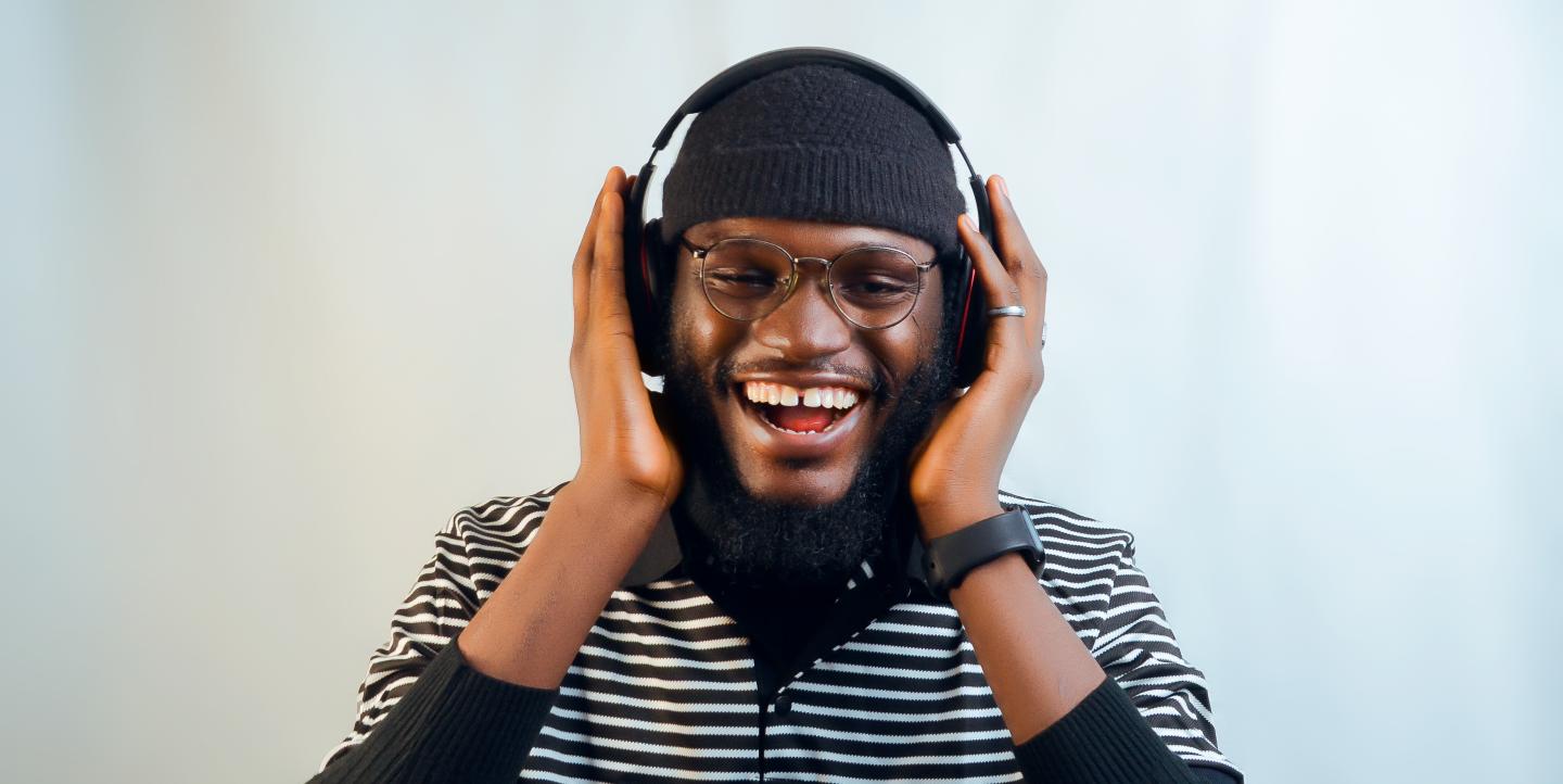 Hombre africano escucha audio con auriculares y sonríe