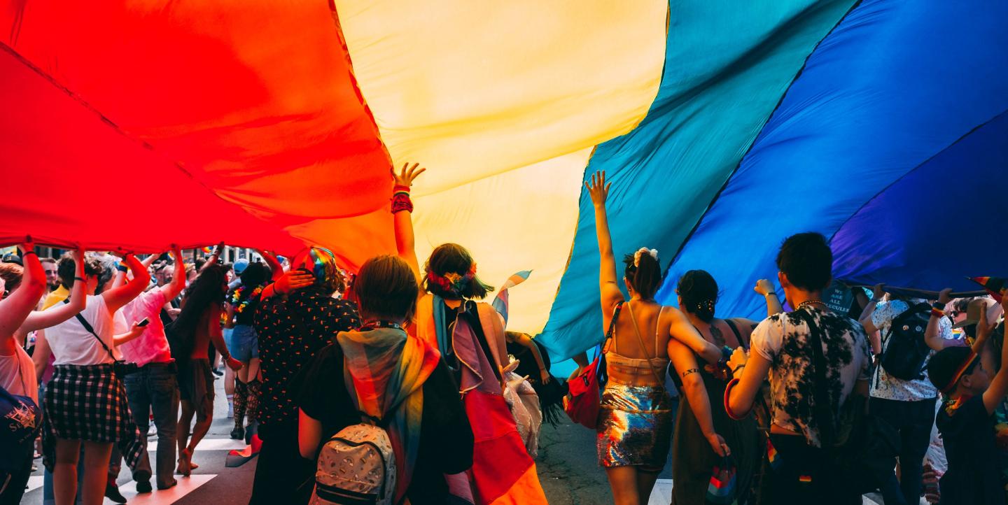 Crowd holding up a large rainbow flag during a Pride march