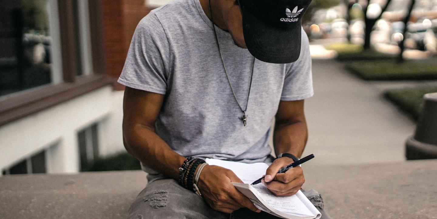 Black man writing in adidas hat