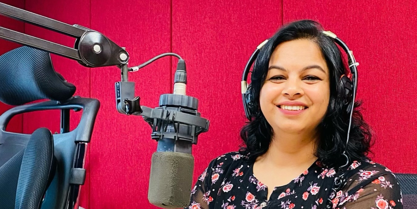 Binita Dahal with headphones on sitting in from of a podcasting microphone