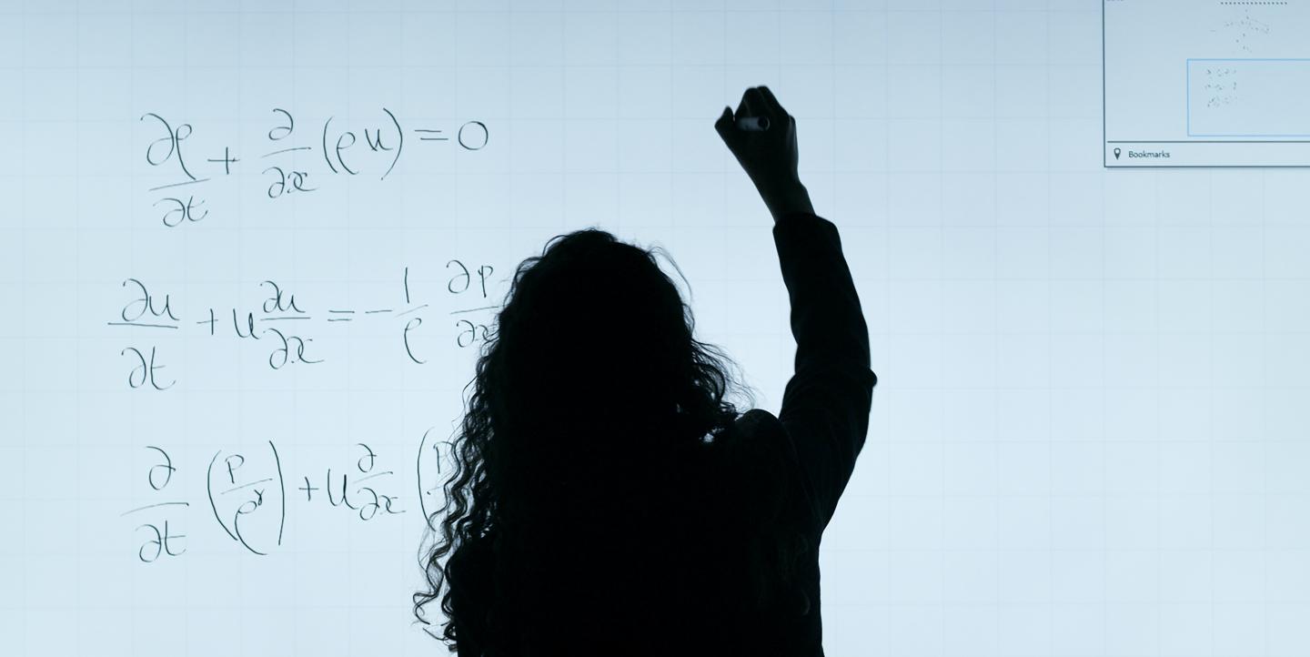 Woman writing math equations on a white board