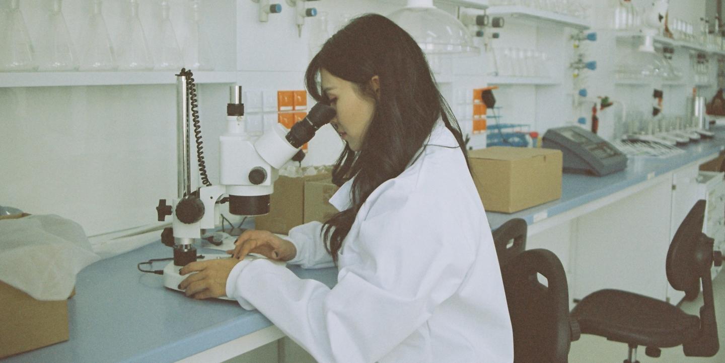 Woman looking at microscope in a lab