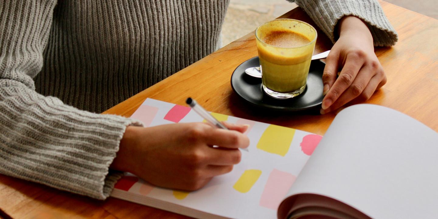 Woman writing in notebook with coffee in hand