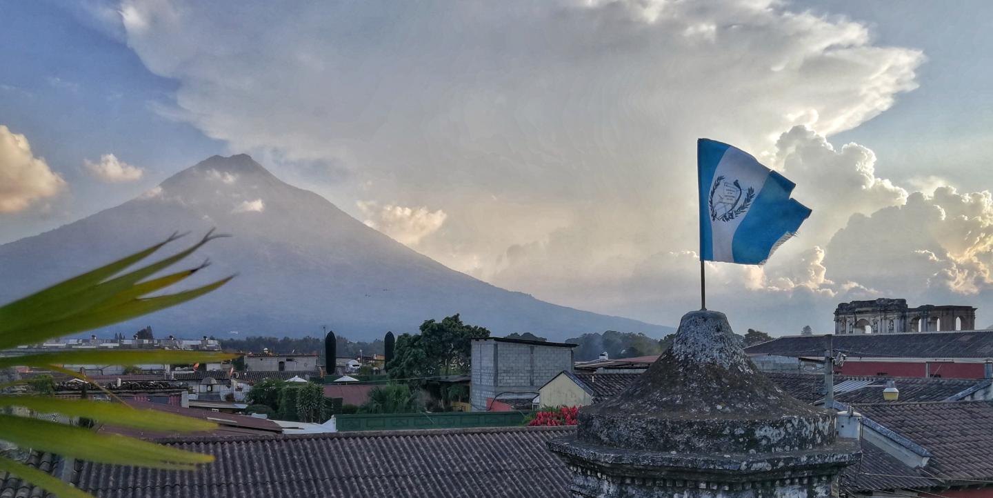 Bandera de Guatemala en lo alto de un edificio con un volcán al fondo