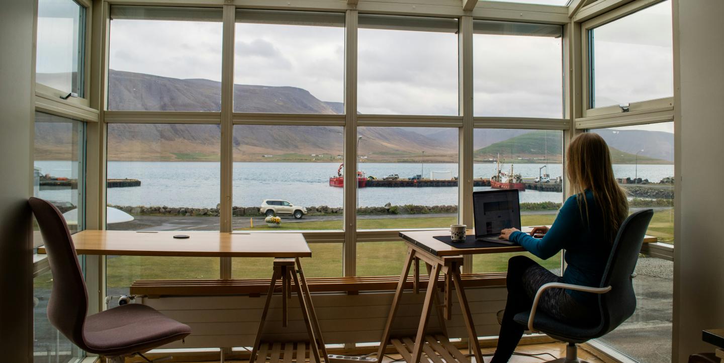Woman working on a laptop in front of a window showing mountains