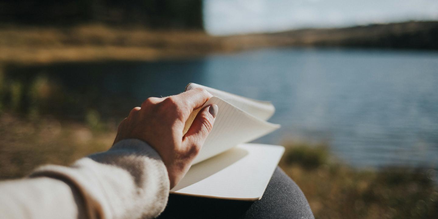 Person holding a notebook in front of a lake