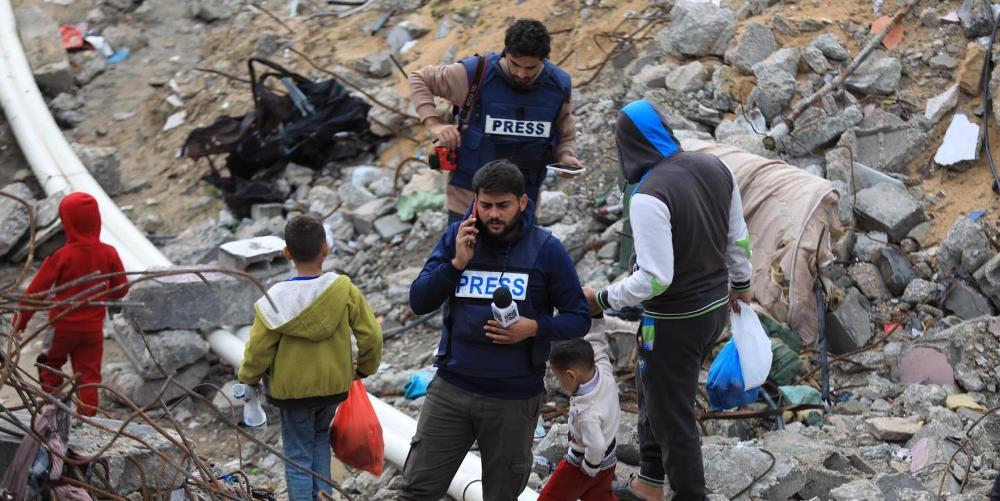 Journalists in Gaza walking amongst wreckage with press jackets on
