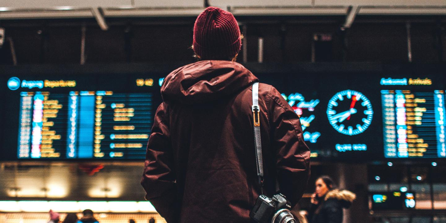 Man with a camera in front of a airport departure board