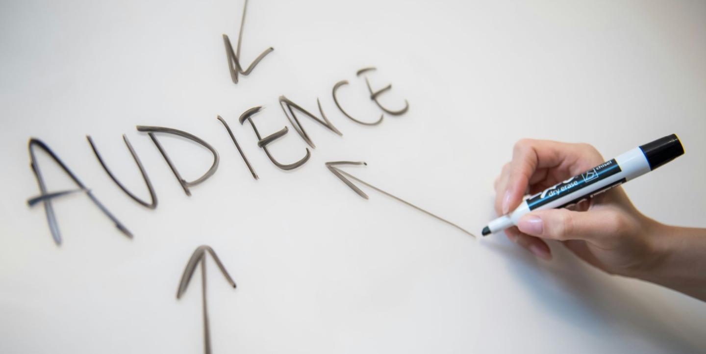 Person writing "audience" on a whiteboard with a black marker