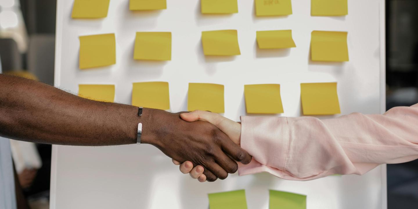 People shaking hands in front of an idea board