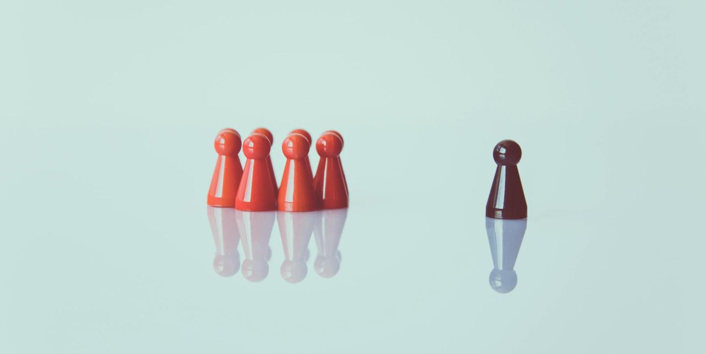 One brown board game piece standing apart from five red pieces