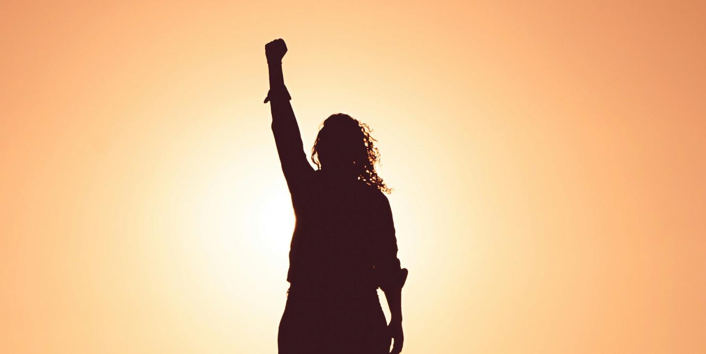 Woman holding fist aloft while silhouetted by the sun