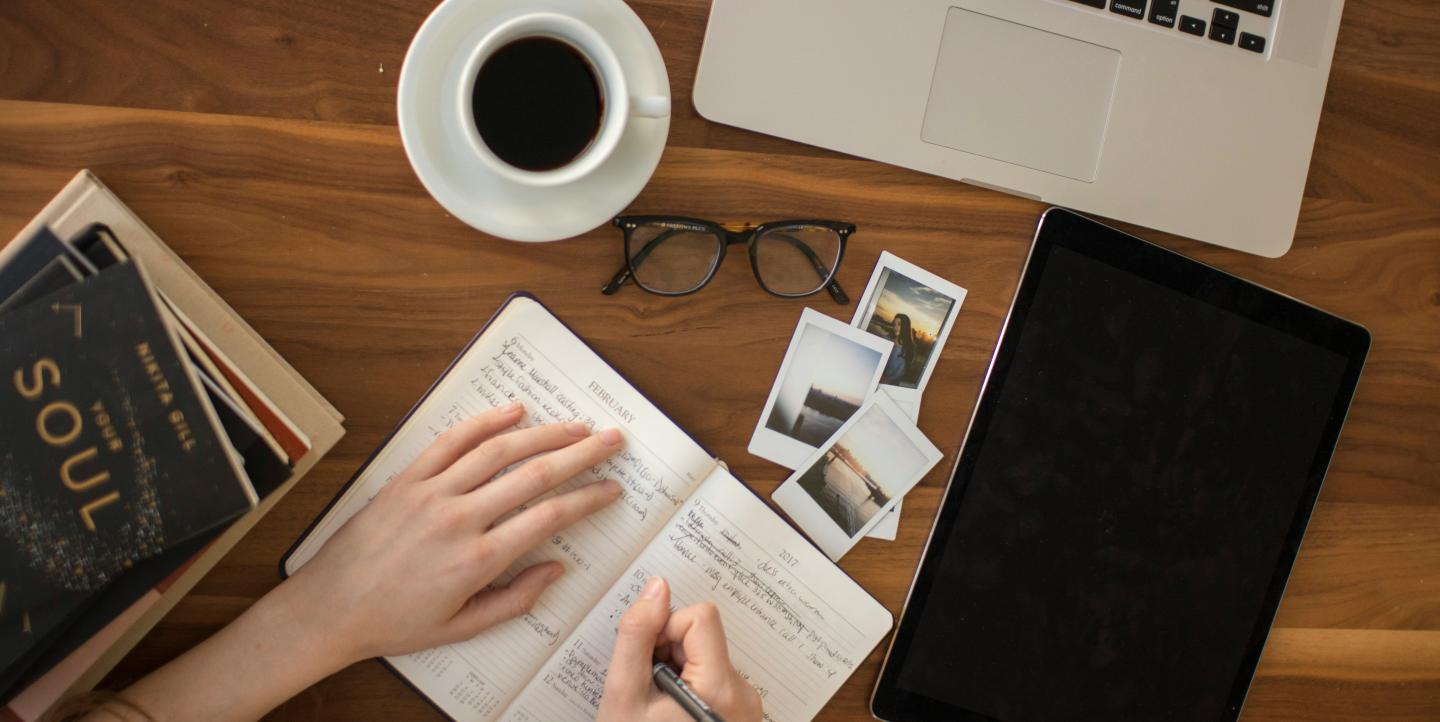 Table de travail d'un jounrliste comportant ordinateur, tablette, cahier de notes et cafe 