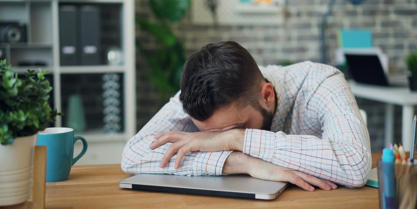 Hombre con la cabeza sobre un escritorio frente a su computadora