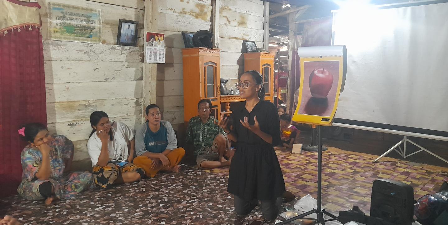 Zulfa in front of an image of an apple speaking to a group of people sitting on the floor