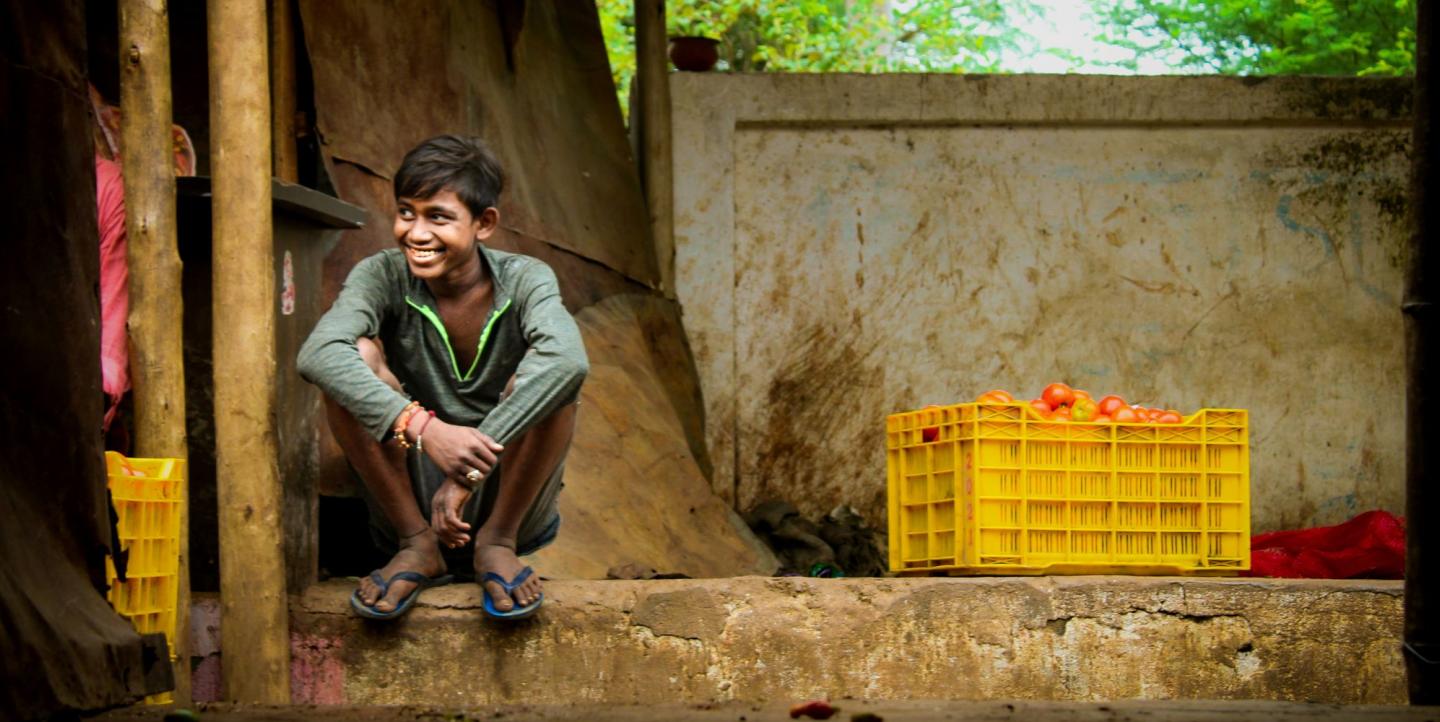 Boy in Chhattisgarh, India sitting by a crate of fruit and smiling