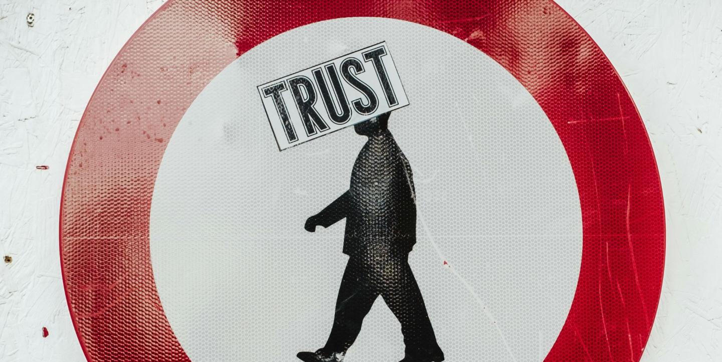 Sign of a man walking with a sticker reading "Trust" over the sign