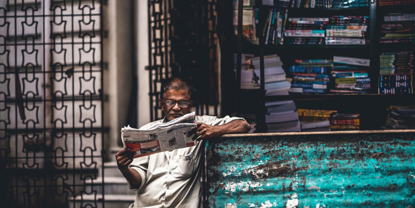 Person reading newspaper in front of a stand in India