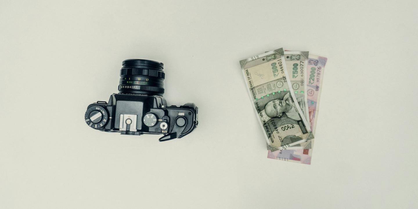 Un appareil photo à côté de quelques rupees sur un fond blanc