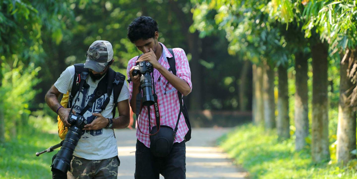 Two men looking at their cameras while in nature.