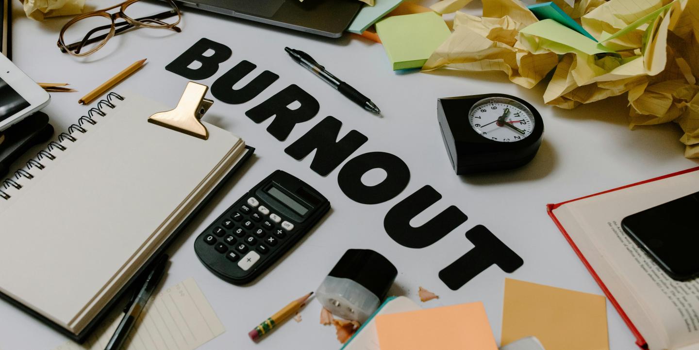 Lots of work supplies and balled up papers scattered over a desk with word burnout in the middle.