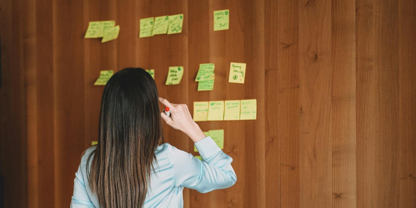 A woman looking at text on sticky notes on a wall.