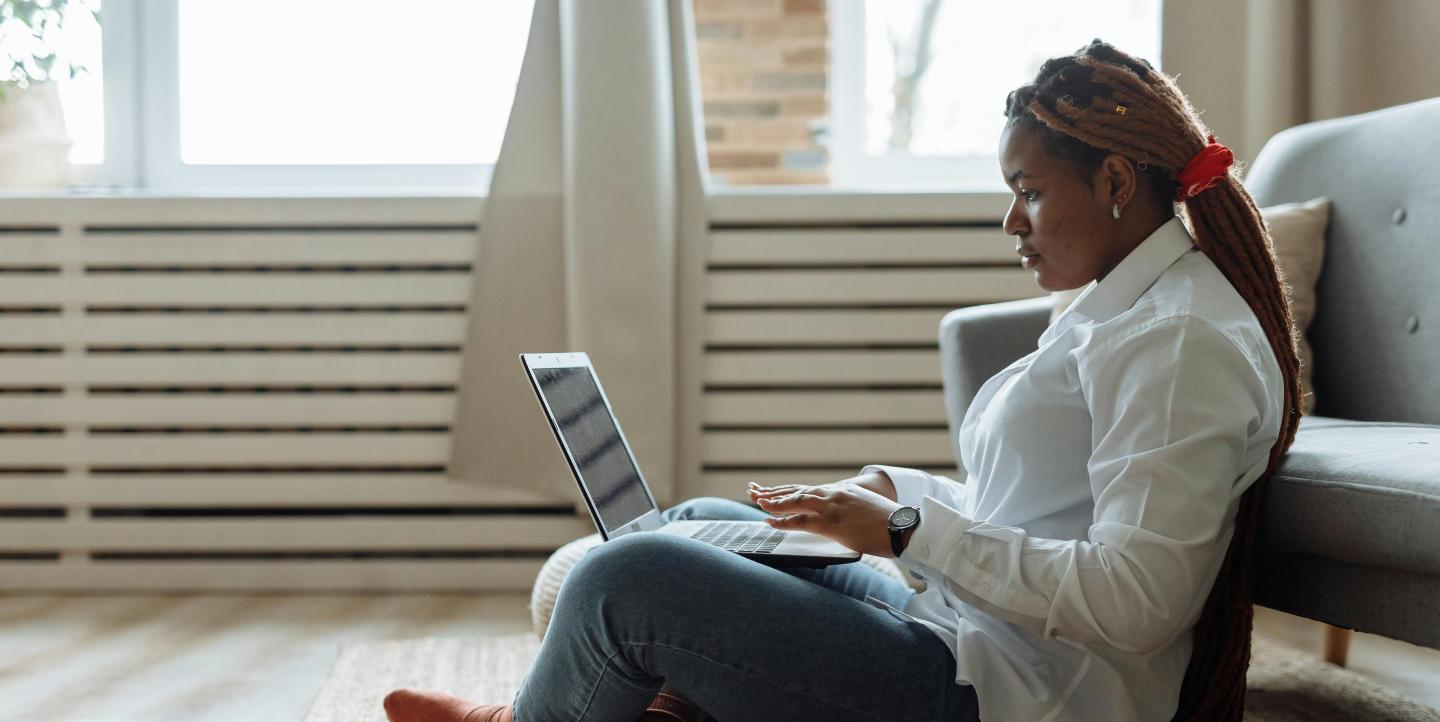 A woman sitting on the floor and working on her laptop. 