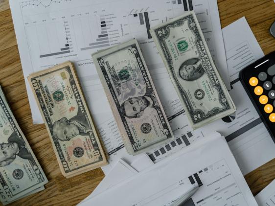 Stacks of money, a calculator on an Iphone and charts 