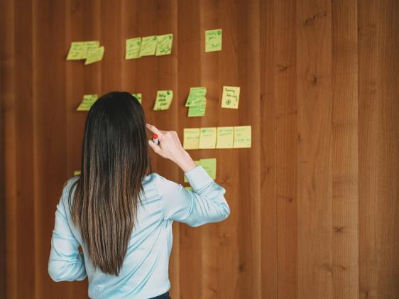 A woman looking at text on sticky notes on a wall.