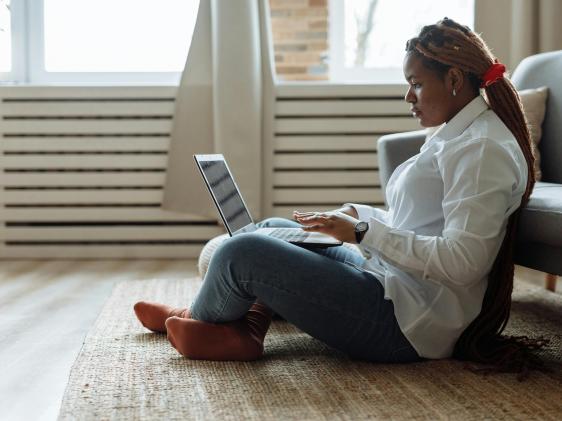 A woman sitting on the floor and working on her laptop. 
