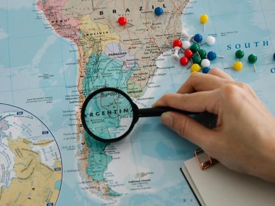 A map of Latin America and a person holding a magnifying glass over Argentina.