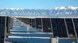 Rows of solar panels on snowy ground in front of mountains