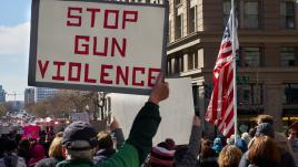 Man carrying a sign at a protest which reads "Stop Gun Violence"
