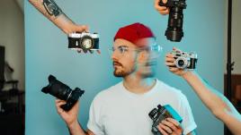 Un photographe, sur fond bleu, avec de multiples appareils photo
